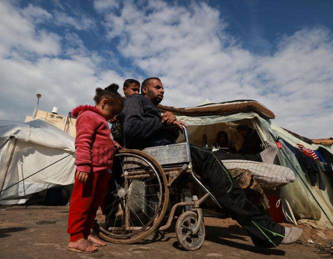 An injured Palestinian man in a wheelchair returns to his tent.