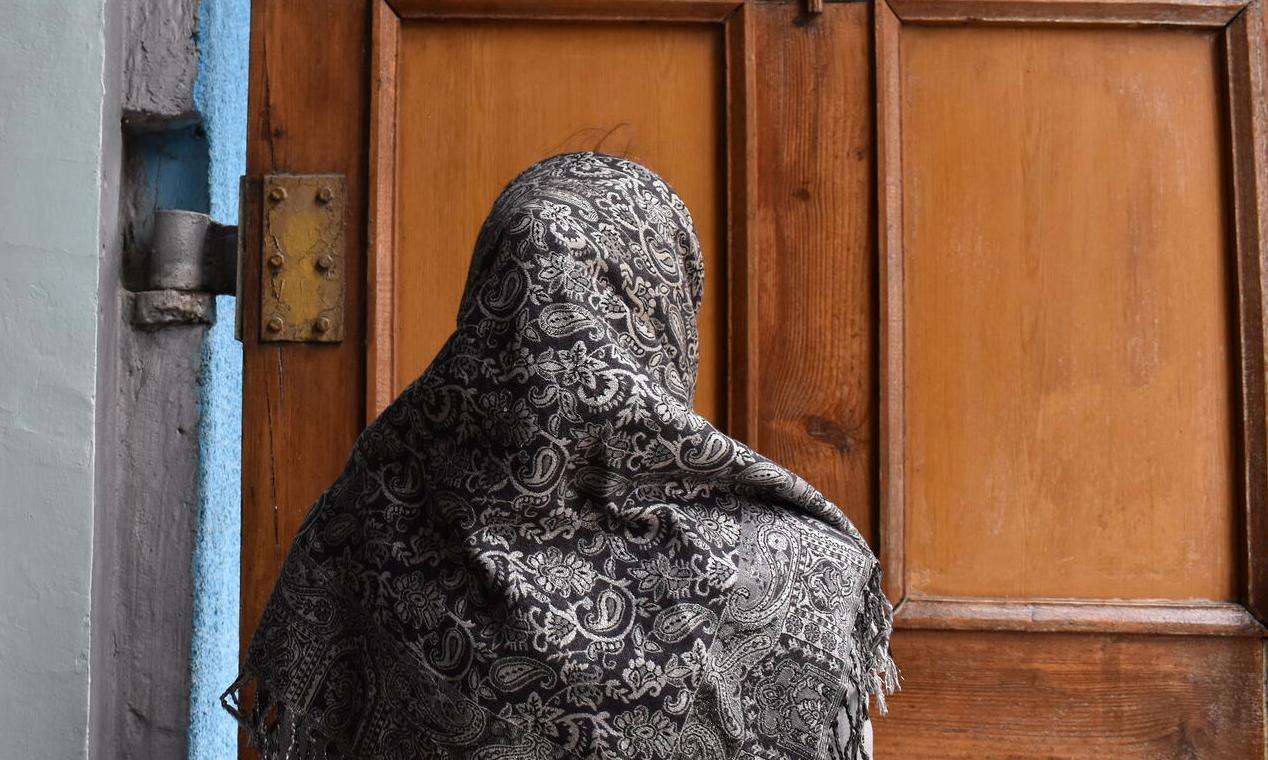 The back of an MSF patient wearing a shawl, standing in front of a wooden door in Belgorod, Russia.