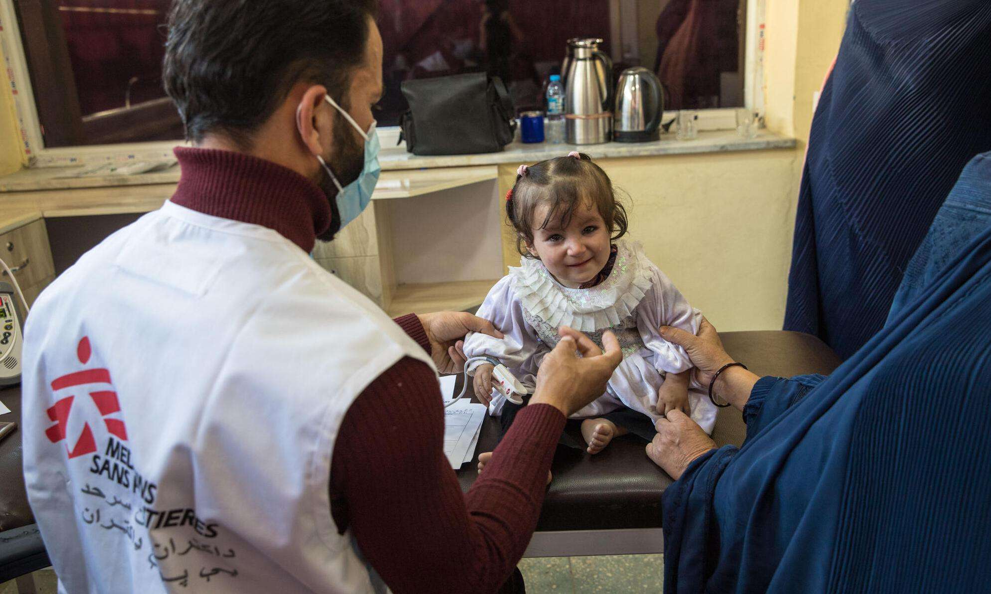 A small child is checked by an MSF staff member with her mother standing beside her in Afghanistan.
