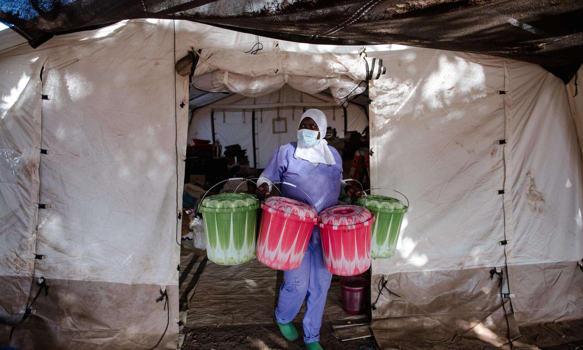 Cisse, a health promoter, carries buckets with kits given to every patient who comes to receive treatment for diphtheria from the logistics tent set up on the ground of the Centre de Traitement Epidemiologique in Guinea.