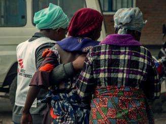 An MSF staff member and two other women link arms in DR Congo.