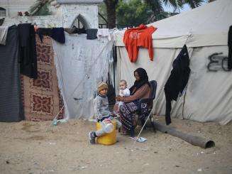 A displaced Palestinian woman with her children outside a makeshift tent in Gaza.