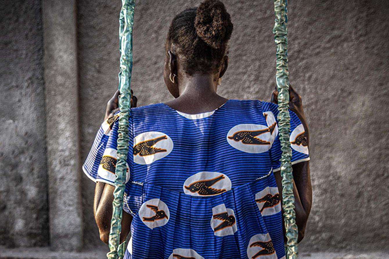 Back of a woman in a blue dress sitting on a swing in the Central African Republic