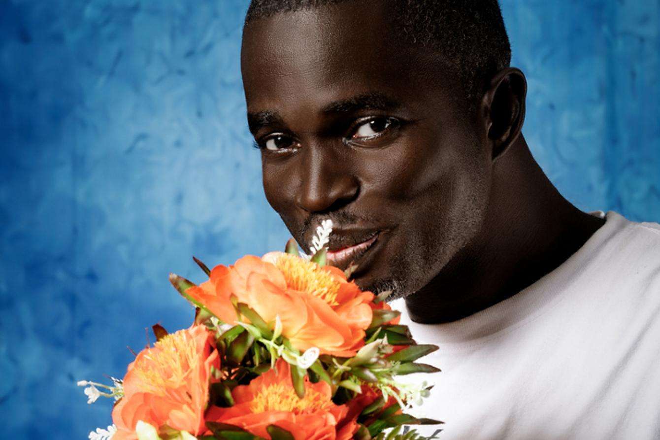A man holding a bouquet of flowers against a blue background.