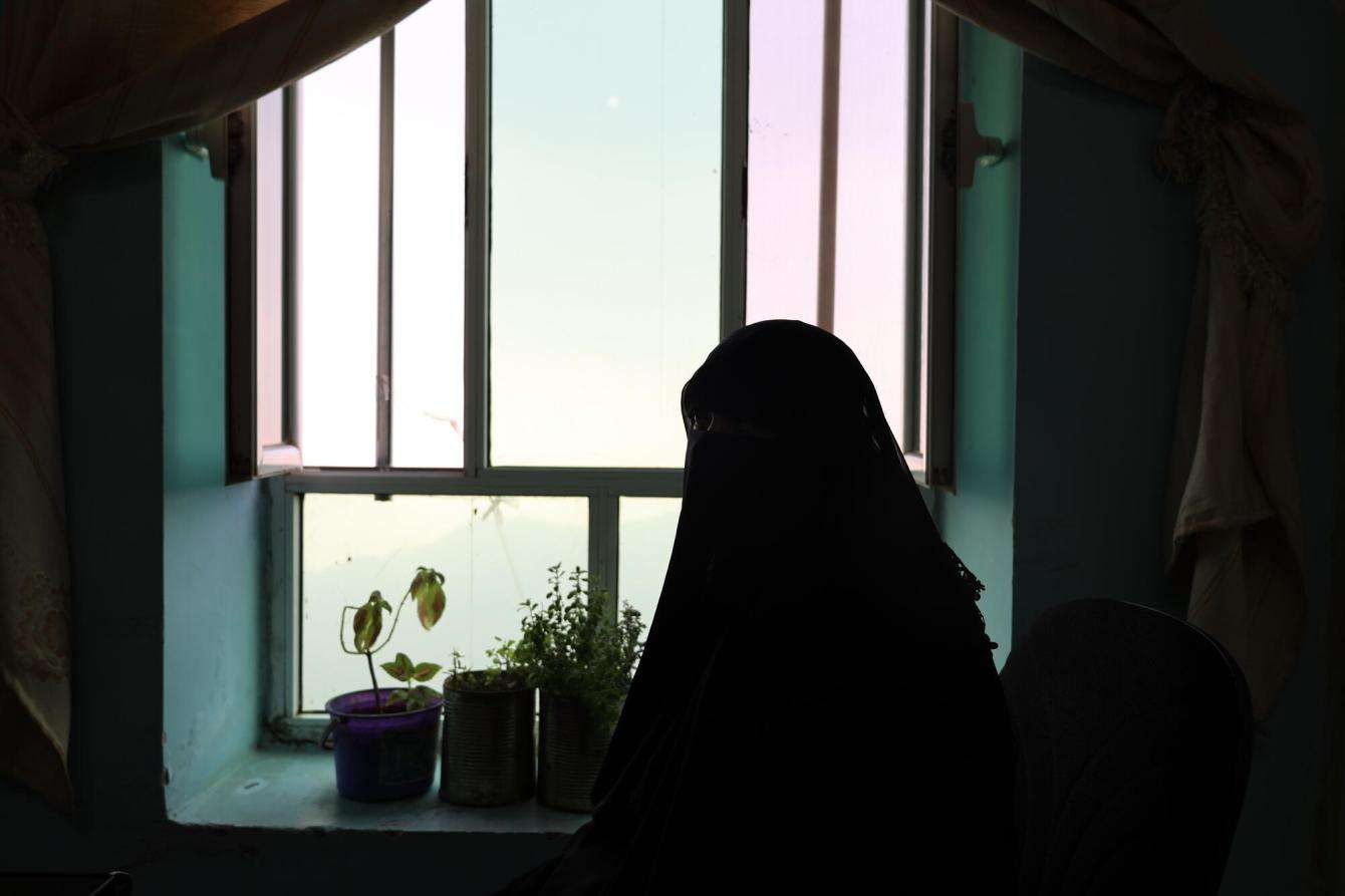 Shadow silhouette of a woman covered in abaya next to a window and houseplants in Yemen