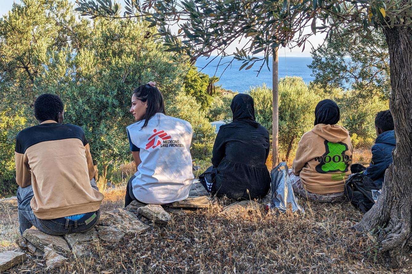 An MSF staff member sits with migrants on a hilltop in Lesvos, Greece.