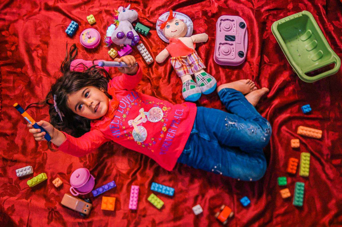 A young Syrian refugee child lies on the floor with her toys around her in Lebanon.
