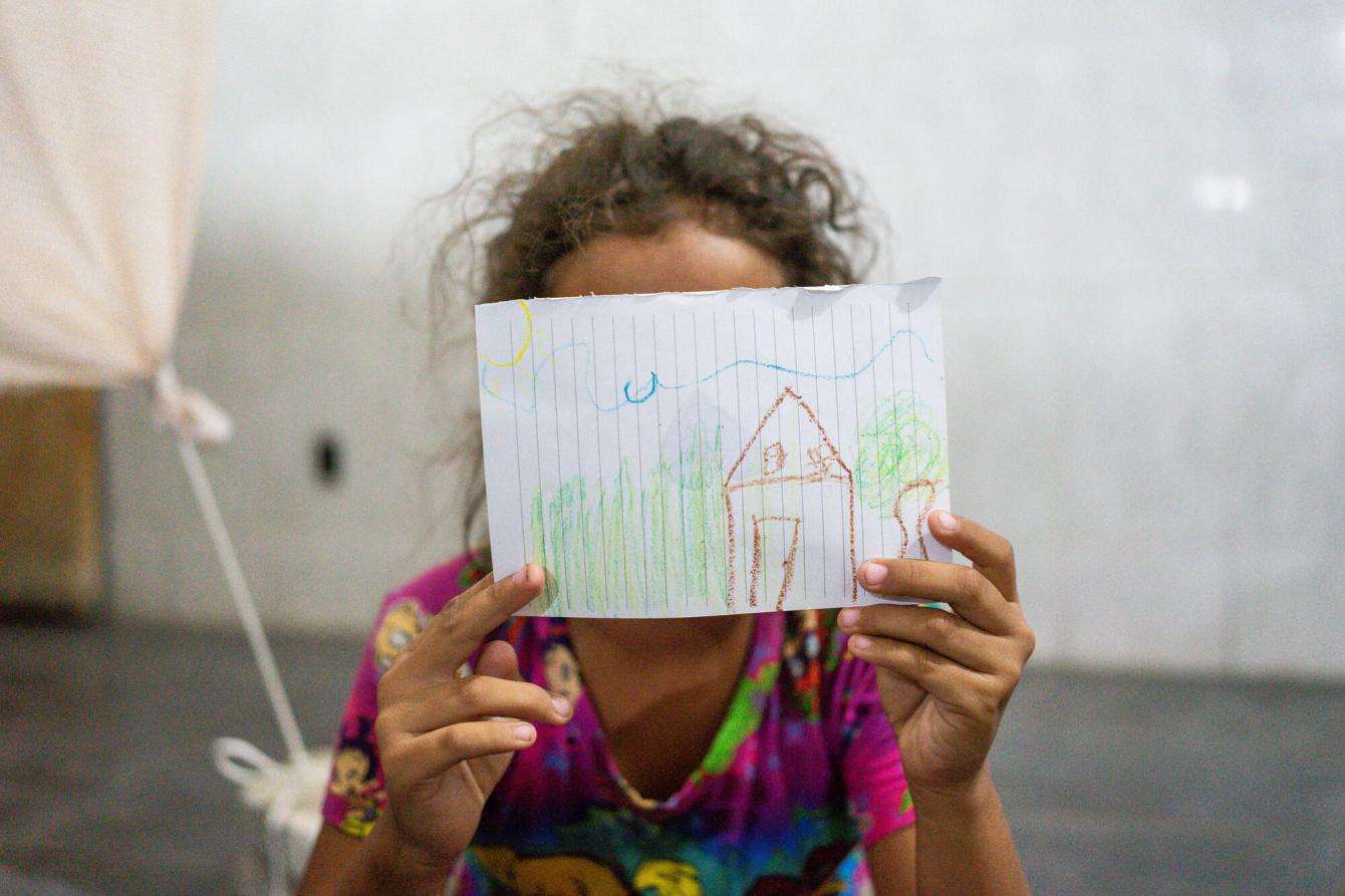 A migrant child holds up a drawing over her face in Mexico