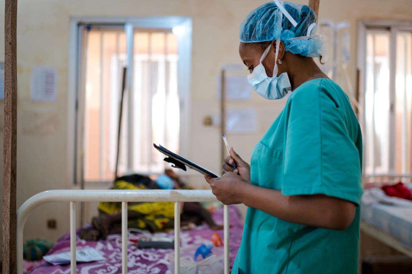 A doctor writes on a pad in a hospital room in Guinea.