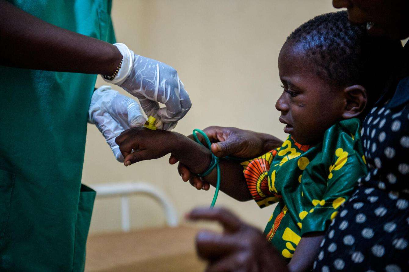 A nurse inserts an IV tube into a child’s hand at the Centre de Traitement Epidemiologique in Guinea.