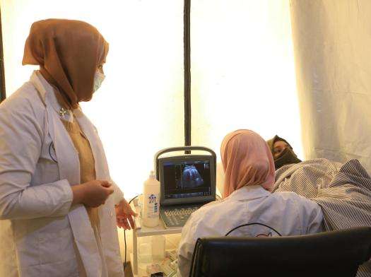 Two women medics are conducting an ultrasound on a pregnant patient in a tented medical room.