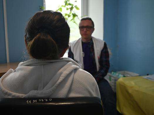 The back of a person sitting in a blue room with an MSF psychologist during an individual therapy session in Ukraine