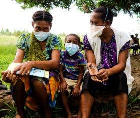 A child sits between two people in surgical masks after completing TB treatment from MSF in Papua New Guinea.